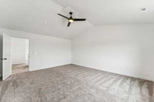 Carpeted empty room featuring vaulted ceiling and a ceiling fan