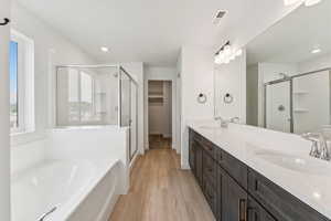 Full bath with a shower stall, double vanity, a bath, wood finished floors, and a spacious closet