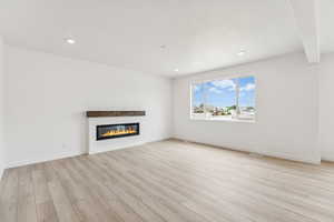 Unfurnished living room featuring a glass covered fireplace, light wood-style floors, and recessed lighting
