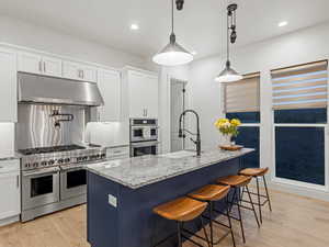 Kitchen with stainless steel appliances, under cabinet range hood, light wood-type flooring, light stone countertops, and recessed lighting