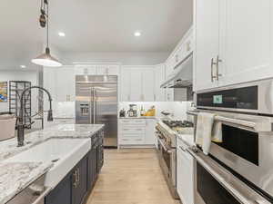 Kitchen featuring white cabinets, high end appliances, hanging light fixtures, recessed lighting, and light stone countertops