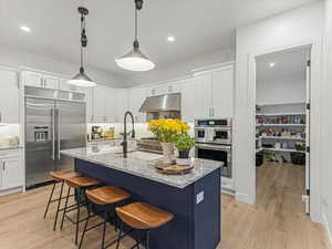 Kitchen featuring stainless steel appliances, white cabinets, light wood finished floors, recessed lighting, and a center island with sink