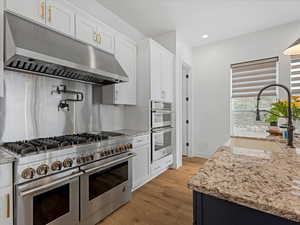 Kitchen featuring appliances with stainless steel finishes, under cabinet range hood, light wood-type flooring, recessed lighting, and white cabinetry