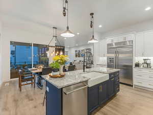 Kitchen with stainless steel appliances, white cabinets, light wood-style floors, an island with sink, and decorative light fixtures