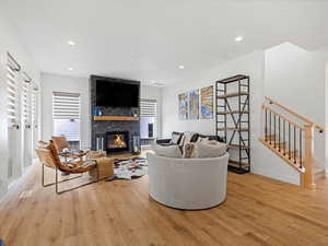 Living room with light wood-style flooring, a large fireplace, recessed lighting, and stairs