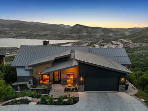 Contemporary home with stone siding, a standing seam roof, a mountain view, an attached garage, and concrete driveway