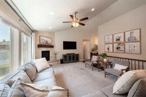 Carpeted living area featuring a stone fireplace, vaulted ceiling, ceiling fan, and recessed lighting