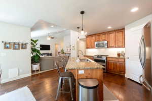 Kitchen with stainless steel appliances, a ceiling fan, light stone counters, dark wood-style floors, and recessed lighting