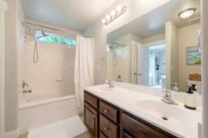 Full bathroom featuring a combined bath / shower with marble appearance and double vanity