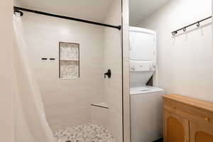 Bathroom featuring stacked washing machine and dryer and a tile shower