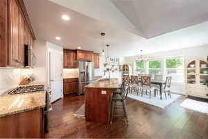 Kitchen with stainless steel appliances, brown cabinetry, a breakfast bar area, light stone countertops, and a chandelier