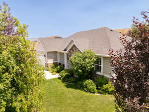 View of front of home with stone siding, an attached garage, a front yard, and roof with shingles