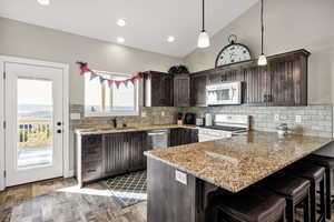 Kitchen featuring white appliances, dark brown cabinetry, a peninsula, wood finished floors, and a kitchen bar