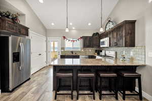 Kitchen featuring stainless steel appliances, dark brown cabinetry, a peninsula, high vaulted ceiling, and recessed lighting