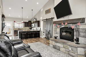 Living area featuring a barn door, high vaulted ceiling, recessed lighting, and a fireplace