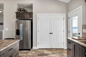 Kitchen with stainless steel fridge with ice dispenser, dark brown cabinets, light wood-style flooring, and light stone counters