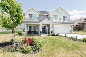 View of front of home featuring stone siding, a garage, concrete driveway, covered porch, and a front yard
