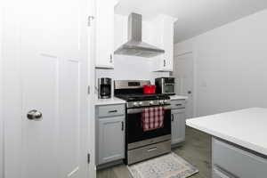Kitchen with wall chimney range hood, gas range, light wood finished floors, light countertops, and gray cabinetry