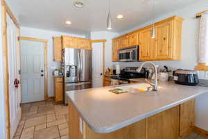 Kitchen featuring appliances with stainless steel finishes, a peninsula, recessed lighting, decorative light fixtures, and light stone finish floors