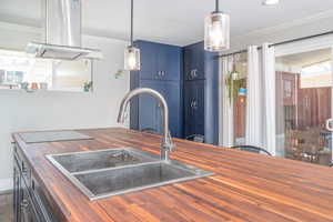 Kitchen with wood counters, blue cabinets, crown molding, island range hood, and decorative light fixtures