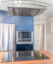 Kitchen featuring appliances with stainless steel finishes, blue cabinets, range hood, ornamental molding, and dark stone counters