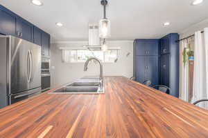 Kitchen with butcher block counters, stainless steel appliances, ornamental molding, recessed lighting, and blue cabinets