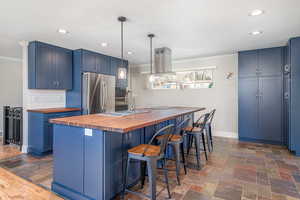 Kitchen with wooden counters, freestanding refrigerator, blue cabinetry, ornamental molding, and recessed lighting