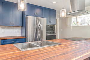 Kitchen with butcher block counters, island range hood, black appliances, blue cabinetry, and ornamental molding