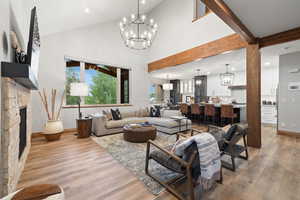 Living area featuring a chandelier, light wood-type flooring, recessed lighting, high vaulted ceiling, and a stone fireplace