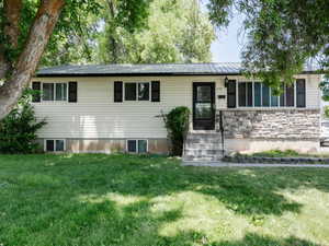 Ranch-style house with a front lawn, a metal roof, and stone siding