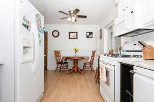 Kitchen featuring white appliances, light wood-style floors, a ceiling fan, white cabinetry, and light stone countertops