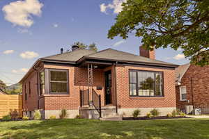 Bungalow-style home with a chimney, a front lawn, brick siding, and a shingled roof