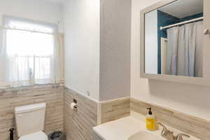 Full bath with vanity, wainscoting, a textured wall, and tile walls