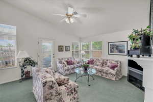 Living room featuring carpet flooring, vaulted ceiling, a ceiling fan, and healthy amount of natural light