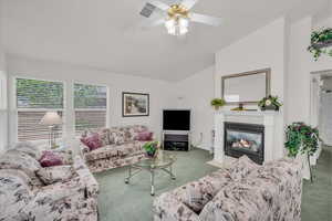 Living room with carpet, lofted ceiling, ceiling fan, and a fireplace with flush hearth