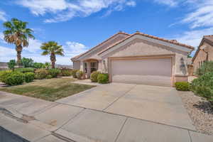 View of front of property with an attached garage, a tile roof, concrete driveway, stucco siding, and a front lawn