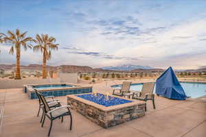 Pool at dusk featuring a hot tub, a mountain view, a community pool, a fire pit, and a patio area