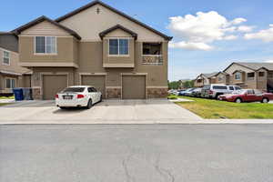 Townhome / multi-family property featuring stucco siding, stone siding, a garage, driveway, and a residential view