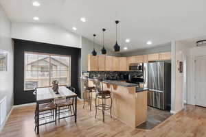 Kitchen featuring appliances with stainless steel finishes, light brown cabinets, a peninsula, dark countertops, and vaulted ceiling