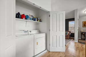 Laundry room with washing machine and dryer and light wood-style flooring