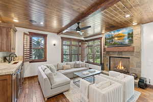 Living area featuring a stone fireplace, wood ceiling, dark wood finished floors, ceiling fan, and wine cooler
