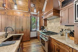 Kitchen with stainless steel stove, custom range hood, decorative backsplash, light wood-type flooring, and brown cabinetry