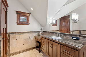 Bathroom featuring vaulted ceiling, tile walls, vanity, tile patterned floors, and wainscoting