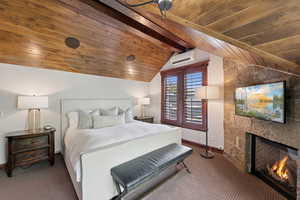 Bedroom featuring carpet floors, an AC wall unit, wood ceiling, and a lit fireplace