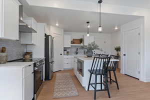 Kitchen featuring stainless steel appliances, white cabinets, a breakfast bar, wall chimney exhaust hood, and pendant lighting