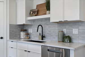 Kitchen with open shelves, decorative backsplash, white cabinetry, light stone counters, and dishwasher