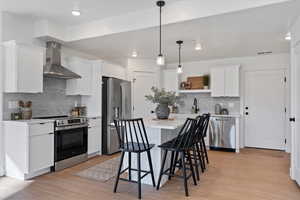 Kitchen featuring stainless steel appliances, wall chimney range hood, hanging light fixtures, white cabinets, and recessed lighting
