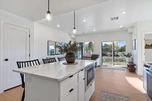 Kitchen with a kitchen breakfast bar, white cabinetry, decorative light fixtures, light stone counters, and light wood-type flooring