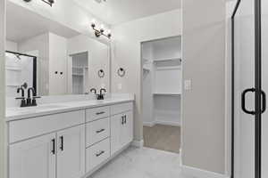 Full bathroom featuring a walk in closet, double vanity, marble finish floors, and a stall shower