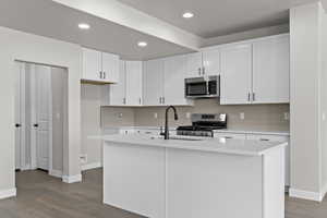 Kitchen featuring appliances with stainless steel finishes, tasteful backsplash, wood finished floors, light countertops, and recessed lighting